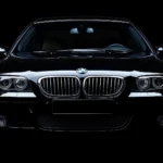 A black BMW M5 in a studio setting with dramatic lighting highlighting its aggressive lines and grille, blending into a seamless black background.