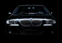 A black BMW M5 in a studio setting with dramatic lighting highlighting its aggressive lines and grille, blending into a seamless black background.