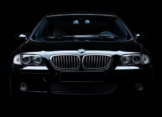 A black BMW M5 in a studio setting with dramatic lighting highlighting its aggressive lines and grille, blending into a seamless black background.