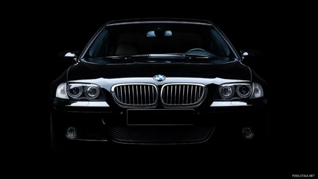 A black BMW M5 in a studio setting with dramatic lighting highlighting its aggressive lines and grille, blending into a seamless black background.