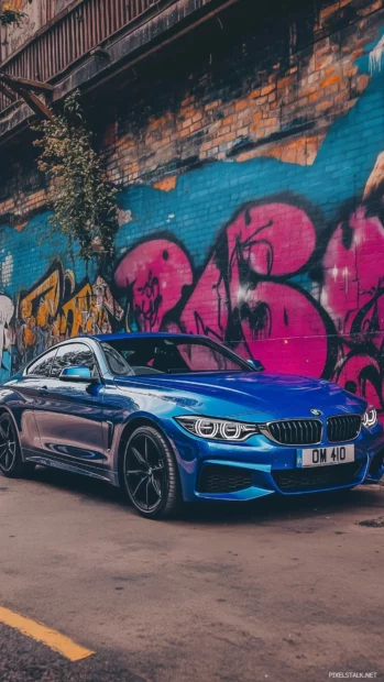 A blue BMW 4 Series coupe parked in an industrial area with vibrant graffiti walls in the background.