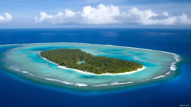 A breathtaking aerial view of a small tropical island surrounded by coral reefs.