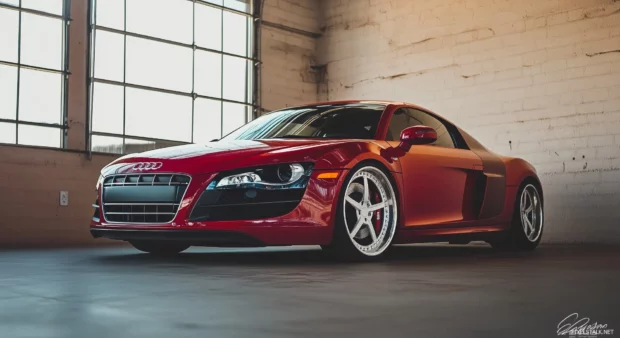 A cherry red Audi R8 parked in a modern industrial space with large windows letting in soft natural light.