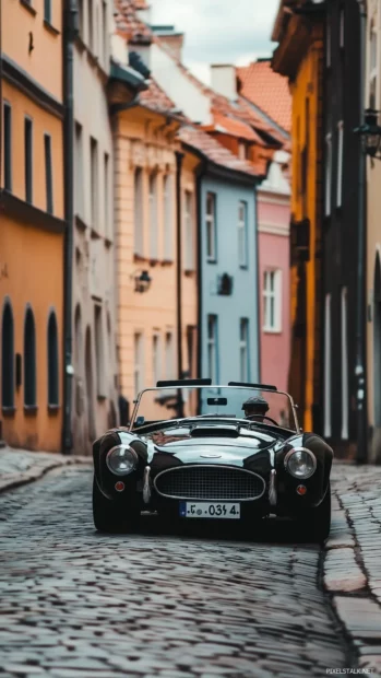 A classic roadster driving through a narrow cobblestone street in a historic European town.