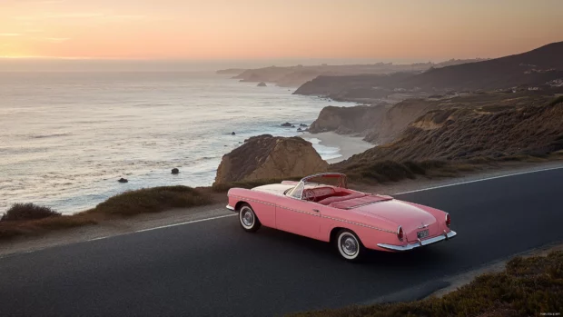 A pink convertible cruising along a coastal road, with the ocean breeze and sunset creating a stunning backdrop.