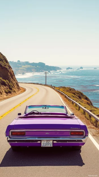 A purple convertible roadster, cruising down a coastal highway with the ocean to one side.