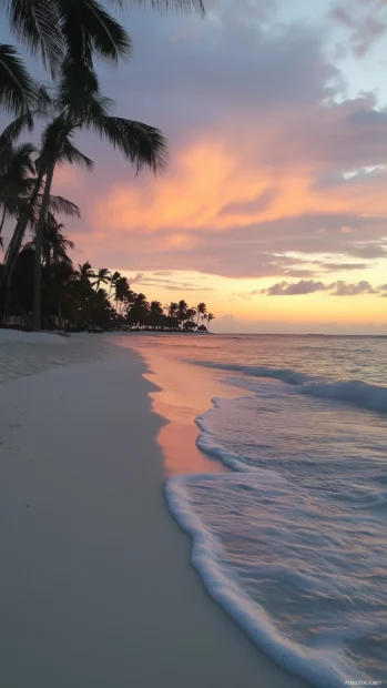 A serene tropical beach at sunset with soft pastel skies blending pink, orange, and purple hues, gentle waves lapping at the white sandy shore.