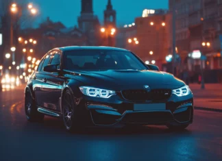 A sleek BMW M3 parked at night on a city street with bright streetlights casting reflections off its glossy black paint.