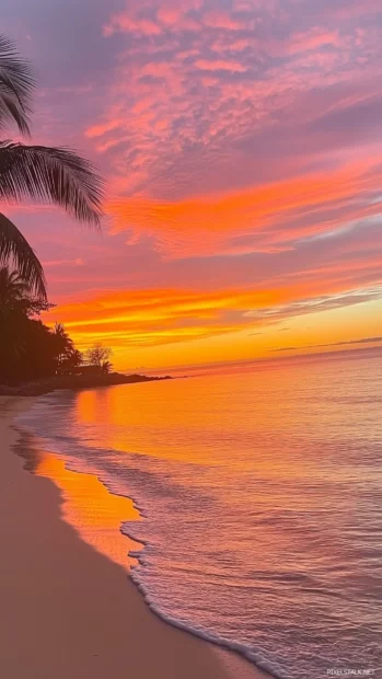 A tropical beach at sunset with dramatic orange, pink, and purple hues in the sky.