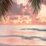 A tropical beach scene with an aesthetic design featuring warm golden hour lighting, palm leaves framing the view, pastel pink and peach skies reflecting on calm water.