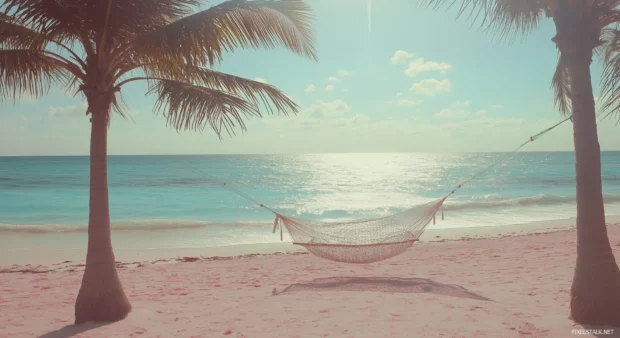 A tropical beach with soft pink sand and crystal clear turquoise water, palm trees swaying in the gentle breeze, a hammock tied between two trees.