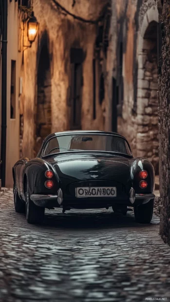 A vintage roadster driving through a narrow cobblestone street in a historic European town.