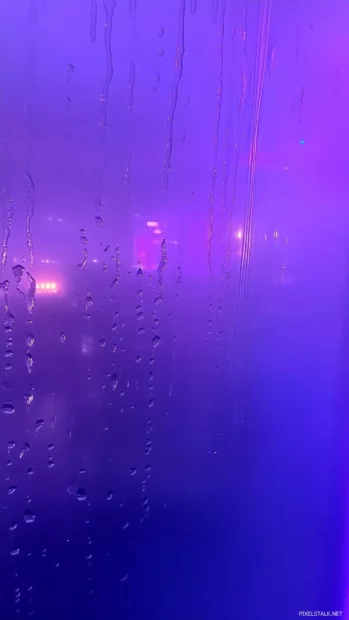 Aesthetic rain wallpaper with Raindrops cascading down a foggy glass window with a soft, blurred view of neon city lights in the background.