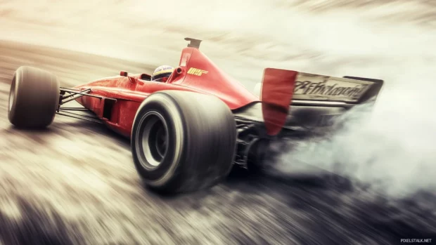 An F1 car drifting through a corner at high speed, with tire smoke and blurred motion in the background.