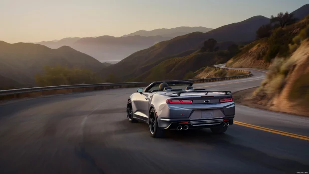 Camaro convertible cruising through a scenic mountain pass during sunset .