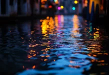 Rain falling on a calm city canal at dusk, water reflecting colorful lights from nearby buildings and streetlamps, ripples gently spreading across the surface.