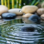 Rain hitting a still water pond in the middle of a Zen garden, soft ripples expanding on the surface, smooth pebbles and green bamboo in the background.