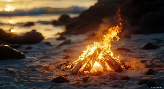 A beach bonfire burning brightly as the sun rises for desktop wallpaper.