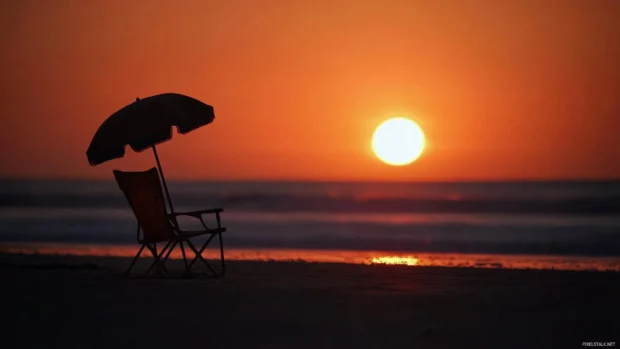 A beach chair and umbrella silhouetted against a breathtaking sunrise.