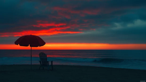 A beach chair and umbrella silhouetted against a breathtaking sunrise wallpaper.