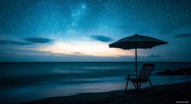 A beach chair and umbrella silhouetted against a starry dark sky (1).