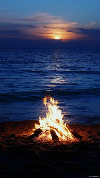 A beach scene at night with a bonfire iPhone wallpaper.