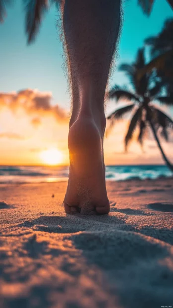 A close up of a person's feet walking on the sand at sunset.