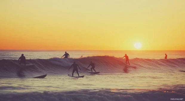 A group of surfers catching the first waves of the day as the sun rises.