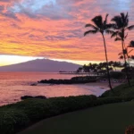 A picturesque sunset at a Hawaii beach with vibrant orange and pink skies reflecting on the ocean .