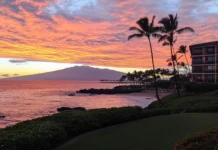 A picturesque sunset at a Hawaii beach with vibrant orange and pink skies reflecting on the ocean .