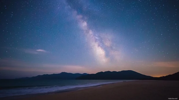 A starry sky above a beach, with the Milky Way galaxy visible in the distance.