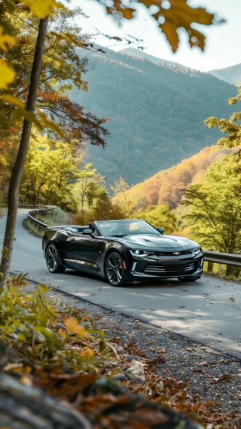 4K Car iPhone Wallpaper with a Camaro convertible speeding through a winding mountain road surrounded by autumn foliage.