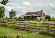 A quaint country farmhouse surrounded by blooming wildflowers and a rustic wooden fence.
