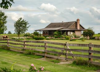 A quaint country farmhouse surrounded by blooming wildflowers and a rustic wooden fence.