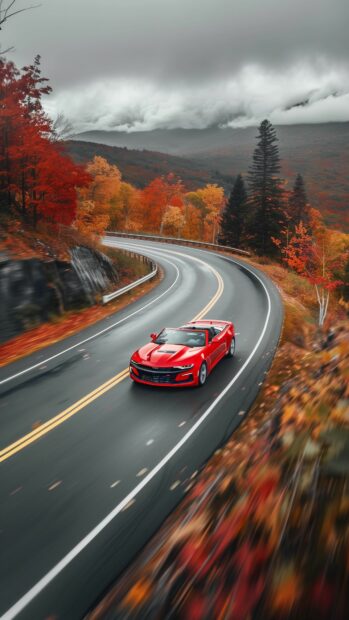 Car iPhone Wallpaper with a Camaro convertible speeding through a winding mountain road surrounded by autumn foliage.