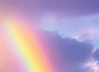 A delicate pastel rainbow stretching across a light, cloudy sky with soft.