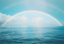 A rainbow over a calm ocean, with gentle waves and a distant horizon, HD background.