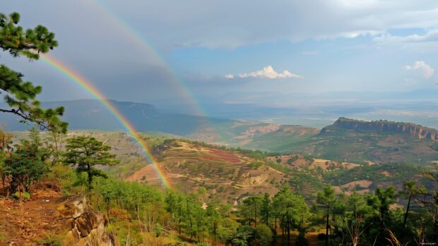 A rainbow seen from a high vantage point, with a wide landscape view below.