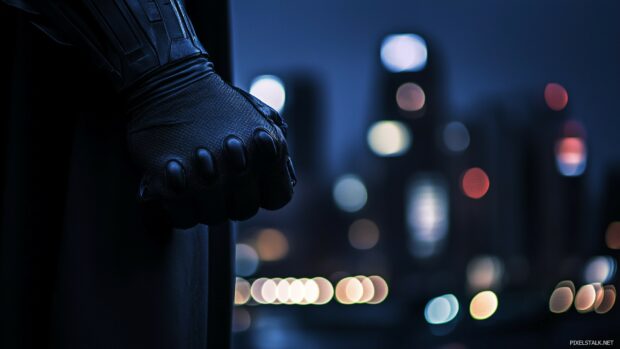 Batman gloved hand holding a Batarang, with Gotham City’s lights in the distance.