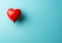 3D Heart shaped balloon floating in a sky blue background.