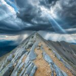 3D Nature with rocky mountain peak with dramatic clouds, sun breaking through, majestic view.