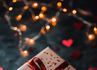 A Valentines gift box wrapped in red ribbon, surrounded by tiny heart confetti and soft fairy lights.