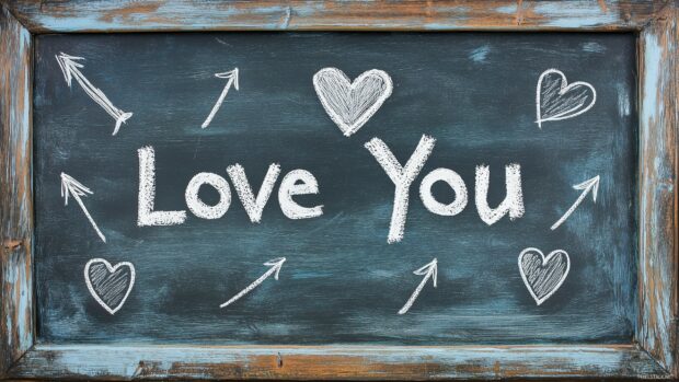 A chalkboard with I Love You written in white chalk, surrounded by doodles of hearts and arrows.