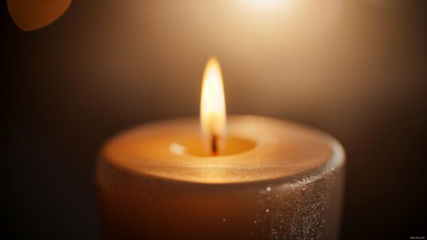 A close up of a candle flame flickering in the dark, casting a warm, gentle light.