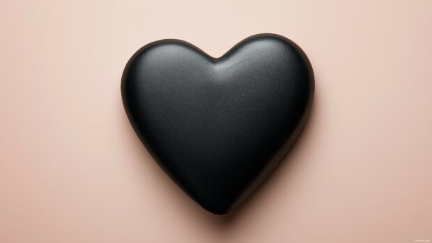 A close up of a matte black heart against a muted pastel background, emphasizing the heart's shape and form.