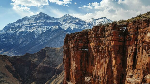 A close up of a rocky cliff face in the Rocky Mountains, with snow capped peaks in the background.