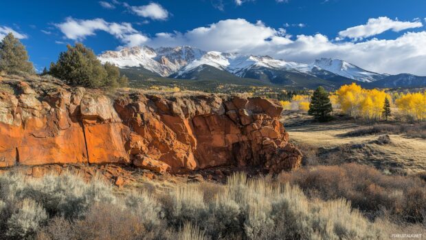 A close up of a rocky cliff face in the Rocky Mountains, with snow capped peaks in the desktop background.