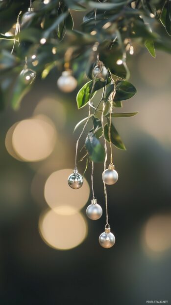 A close up of elegant Christmas ornaments hanging from a lush green tree, with a warm, bokeh background.