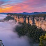 A dramatic mountain landscape desktop wallpaper with layers of fog rolling over rocky cliffs at sunrise.