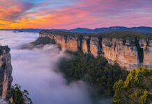 A dramatic mountain landscape desktop wallpaper with layers of fog rolling over rocky cliffs at sunrise.